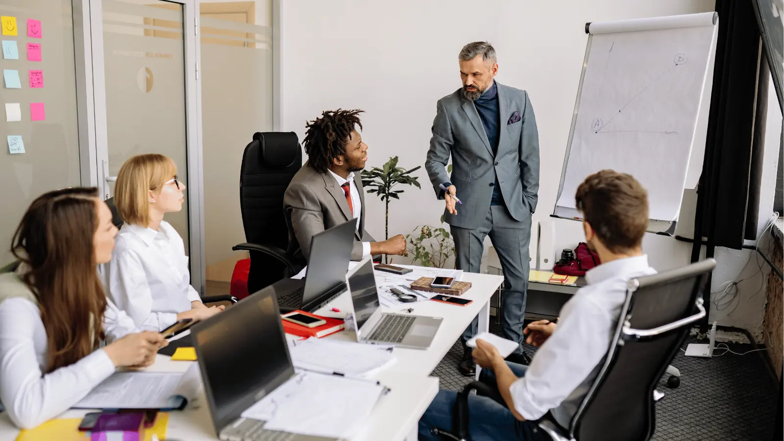 Business team meeting with presenter pointing at colleagues around a laptop-filled table