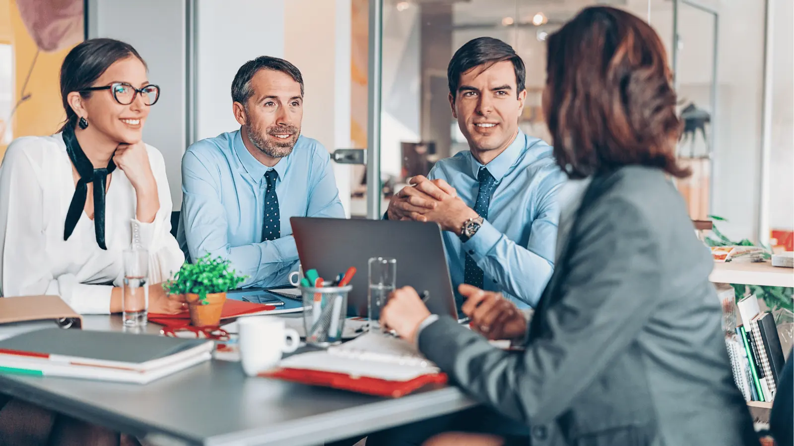 Four colleagues in a bright office meeting around a laptop and documents for scheduling