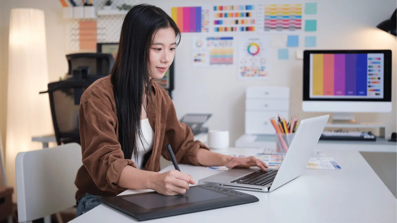 Woman using graphics tablet and laptop at a color-design workspace