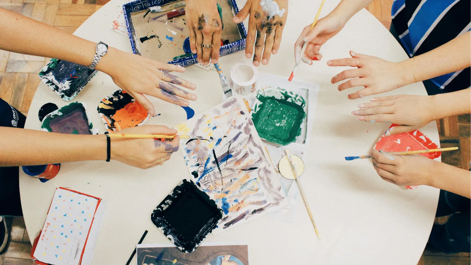 Overhead view of multiple hands painting with brushes on a round table