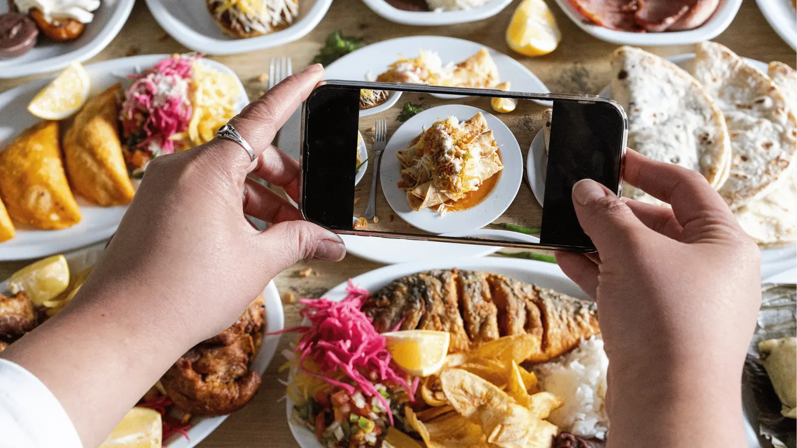 Hands holding smartphone photographing plated Latin-style meal on wooden table