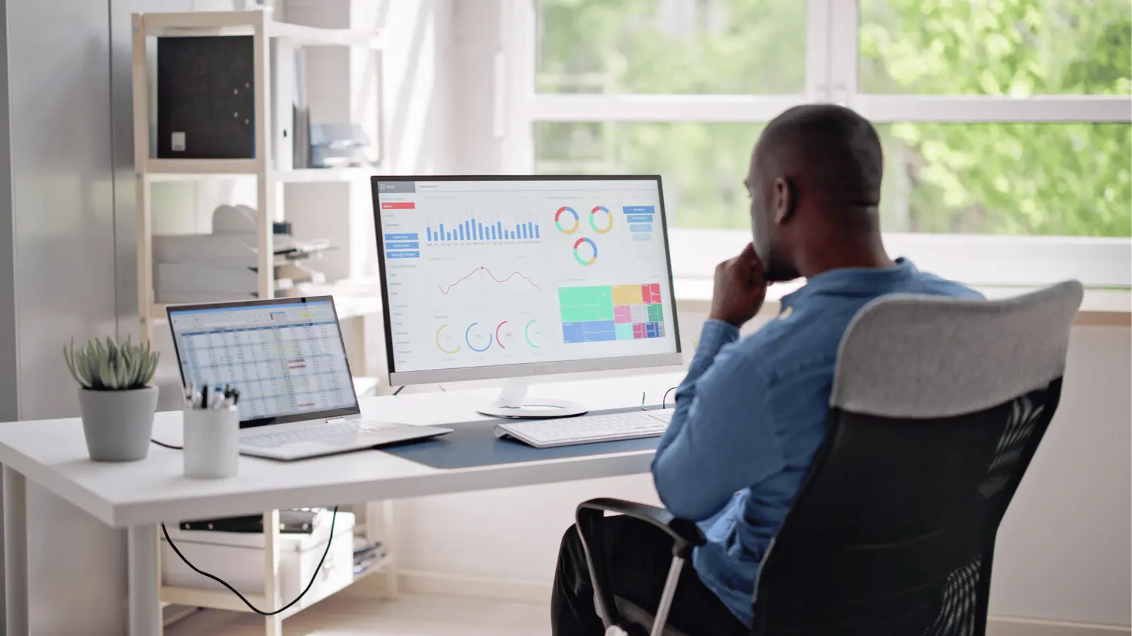 Man sitting at desk looking at analytics dashboards on dual monitors