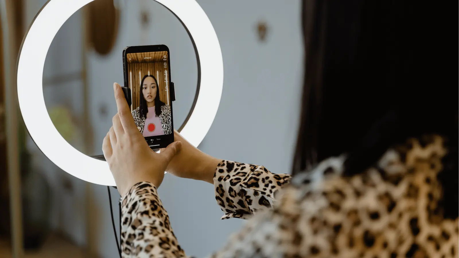 Person holding smartphone in ring light recording a selfie video wearing leopard print