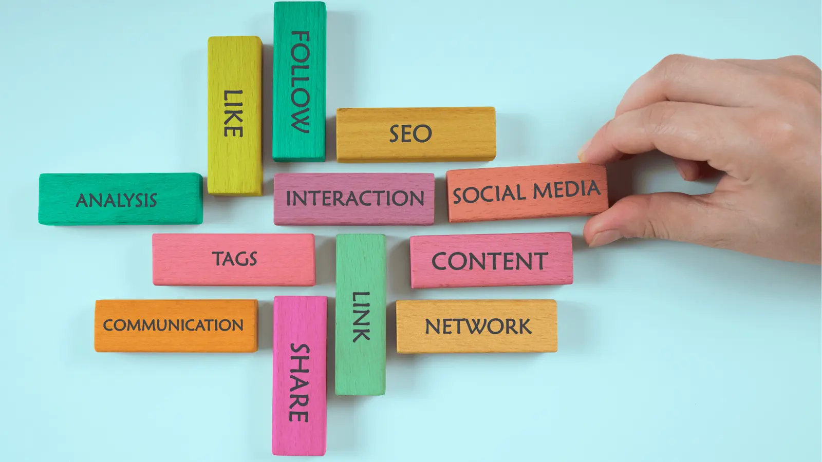 Hand arranging colorful wooden blocks labeled social media and content on blue background for content calendar