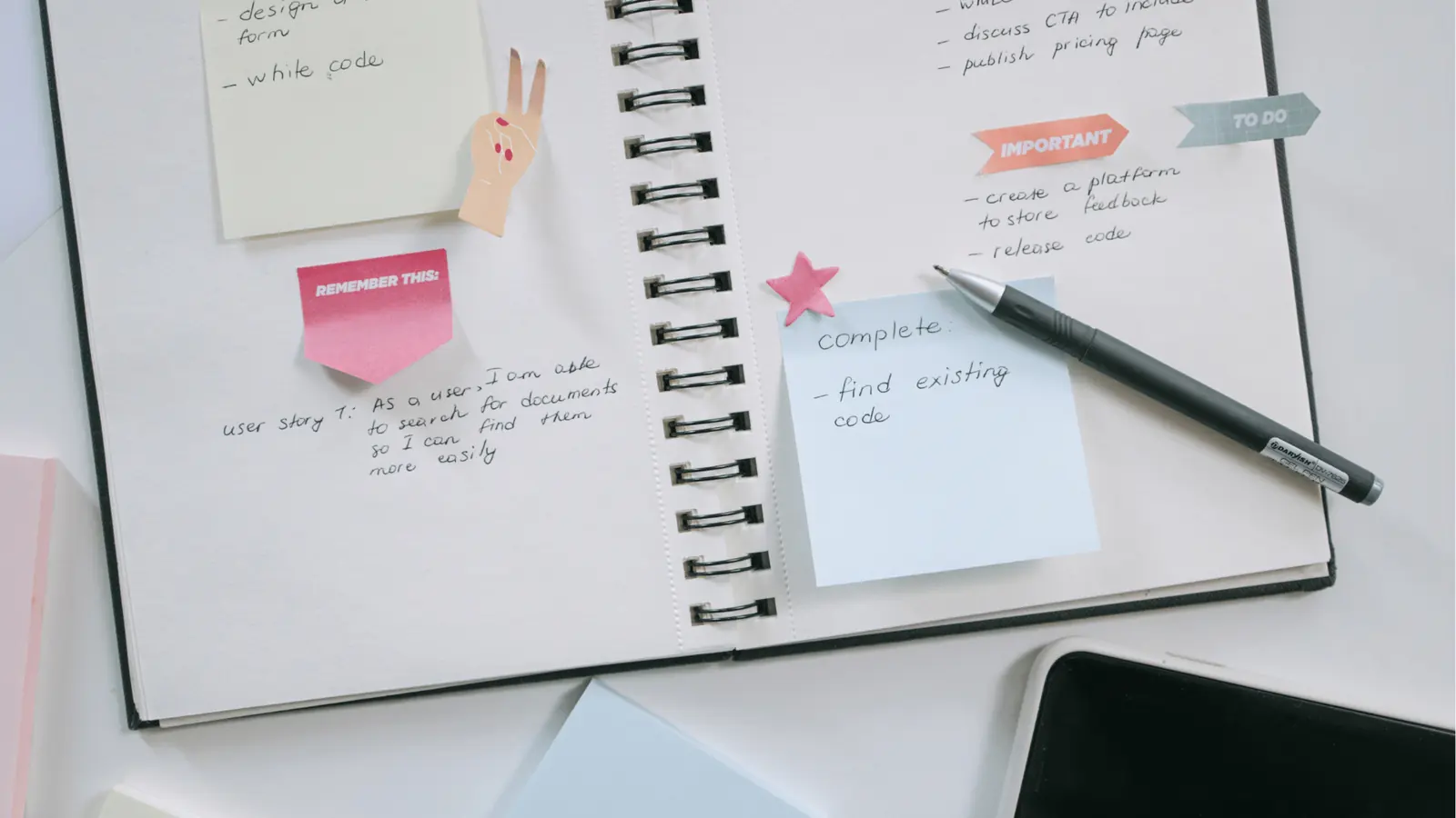Open spiral notebook with sticky notes, pen, and handwritten to-do notes