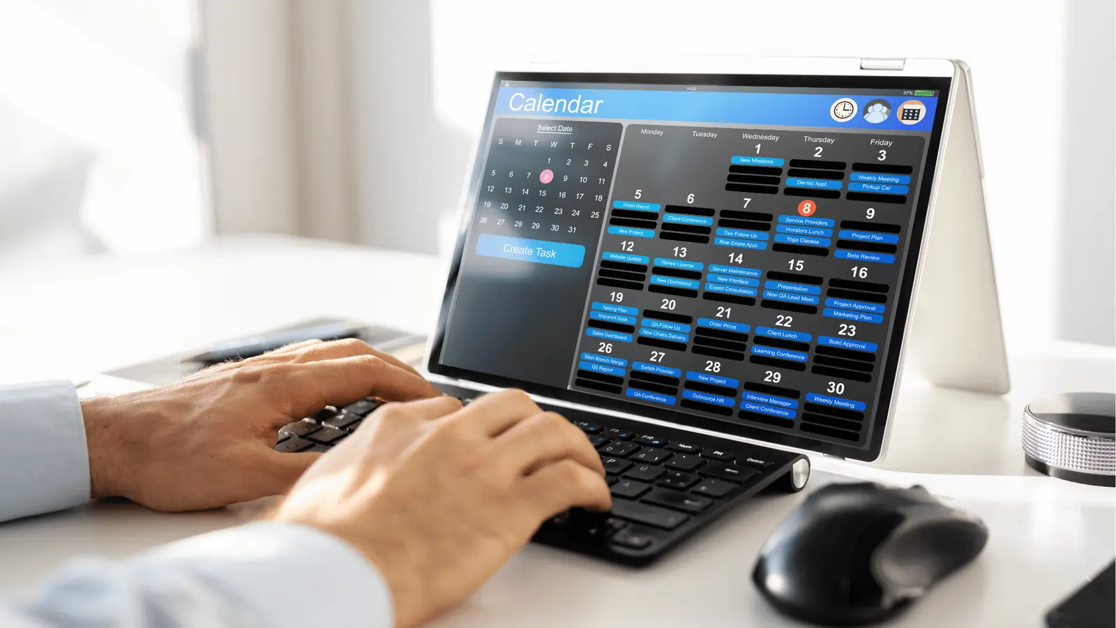 Person typing on keyboard next to tablet showing a monthly calendar app