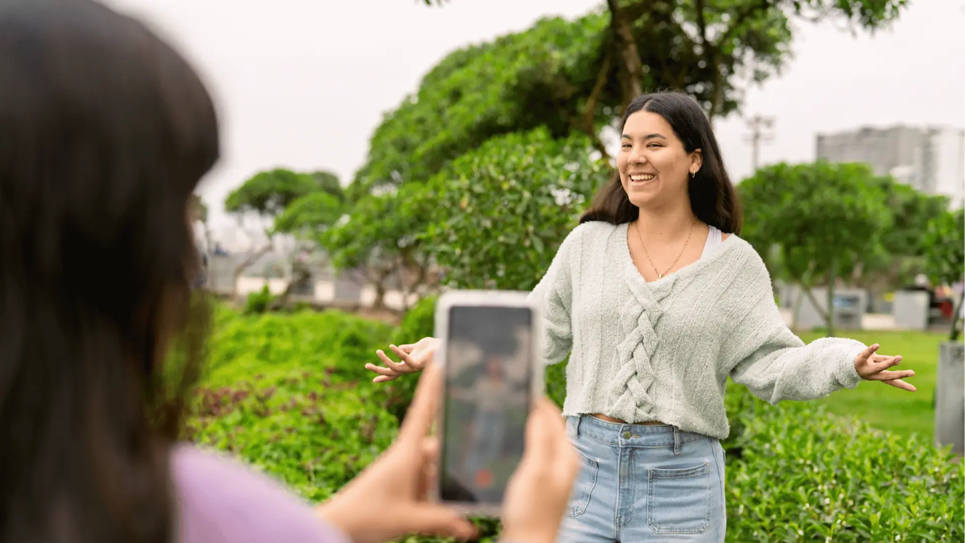Young woman smiling with arms open while friend films her on phone