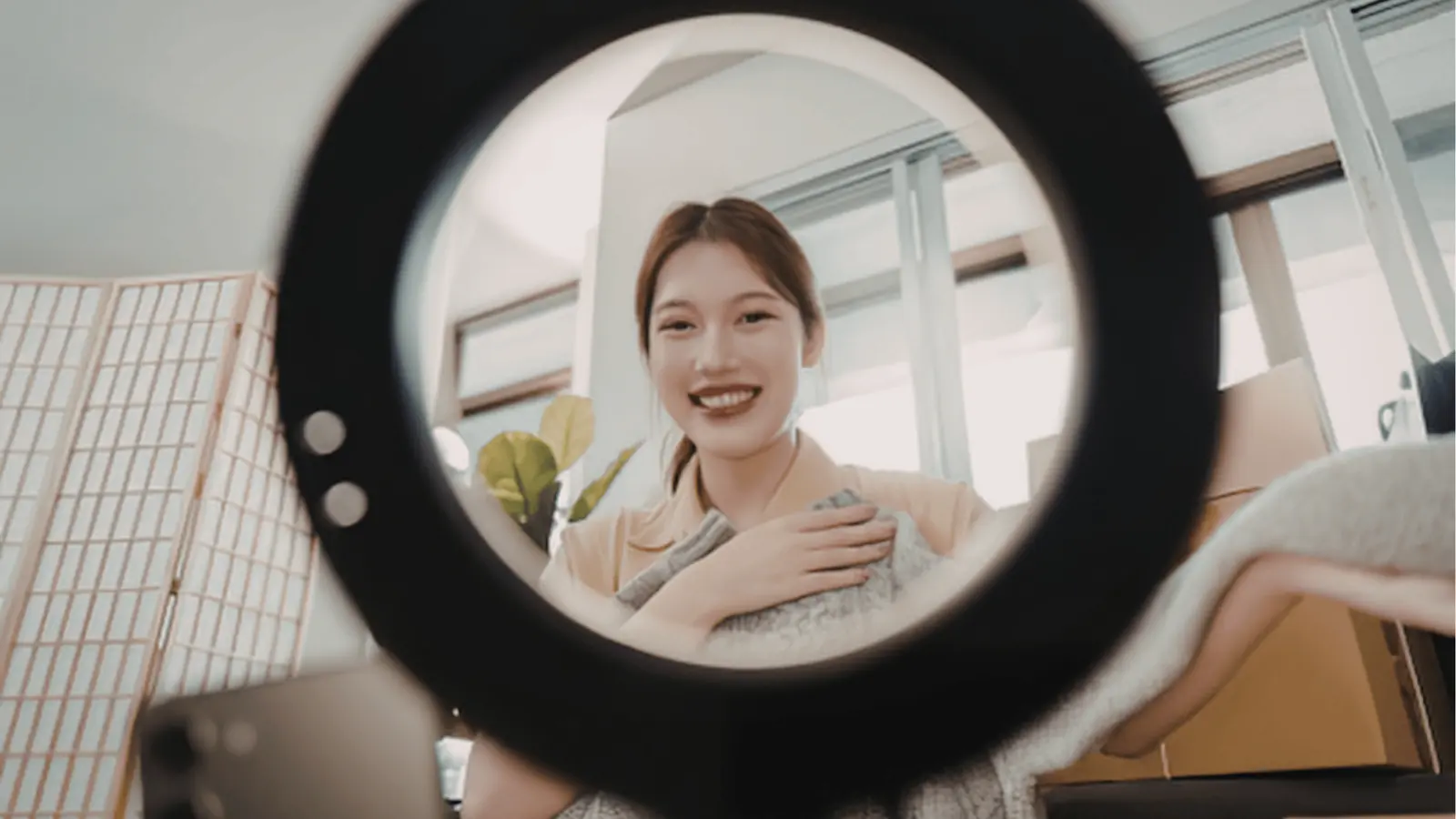 Young woman smiling at camera through ring light while holding a blanket for analytics