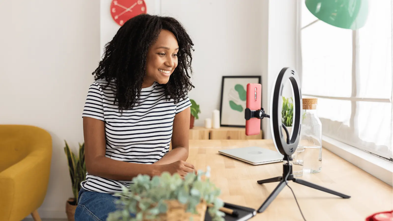 Smiling woman recording on smartphone with ring light at home desk