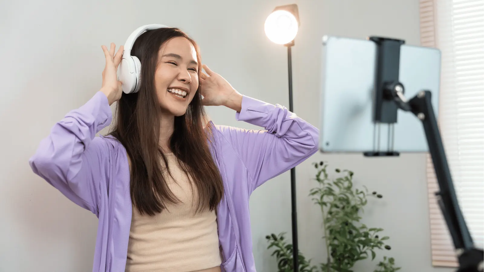 Young woman smiling wearing headphones while recording on a tablet for multi-brand management