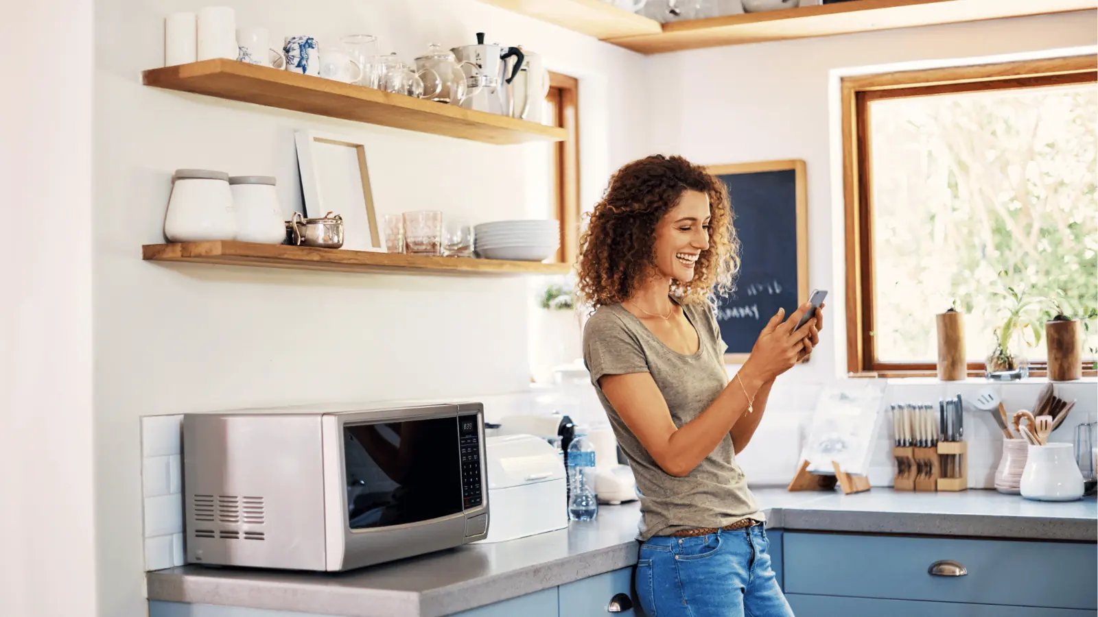 Woman leaning on kitchen counter smiling while looking at her smartphone