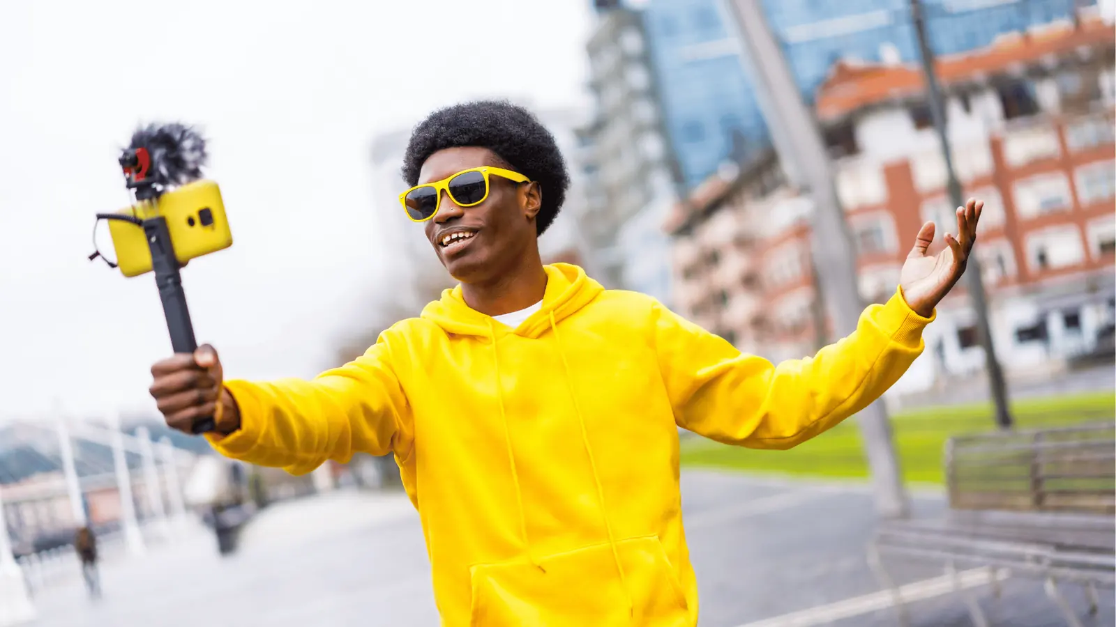 Young man in yellow hoodie vlogging outdoors with phone on handheld gimbal